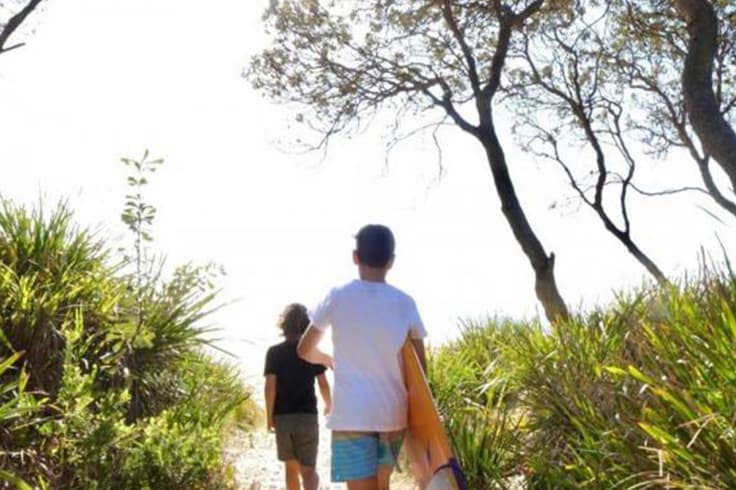 our favourite big4 3 2 people walking to a beach with a surfboard