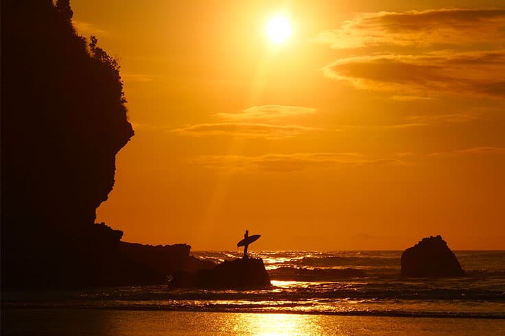 Surfer standing on rock on West Coast beach Surfer standing on rock on West Coast beach